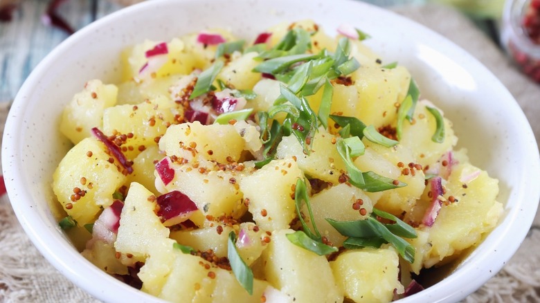fresh potato salad topped with chives and bacon bits in a white bowl