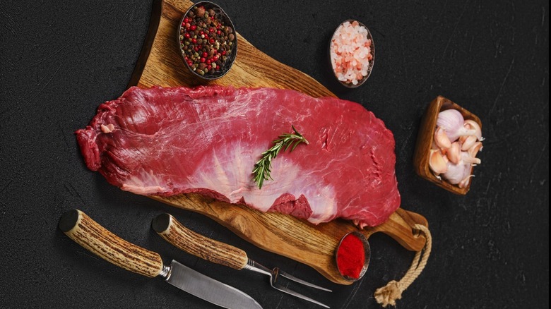 Top view of a ribeye chuck or ribeye cap, surrounded by ramekins of peppercorns, salt, and garlic.