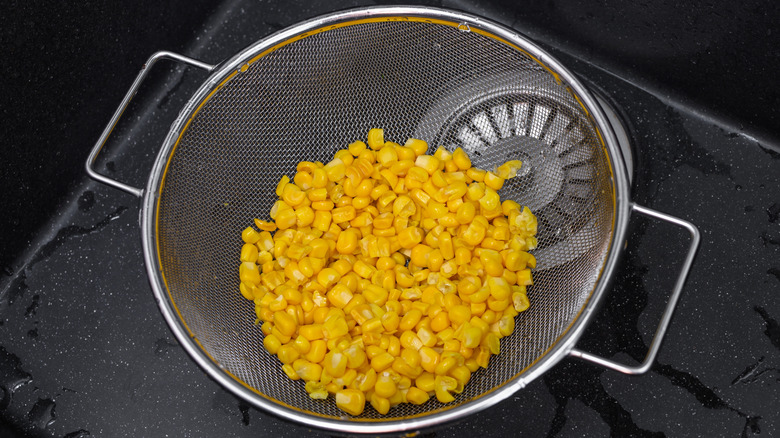 Canned corn in a sieve rinsed in a sink