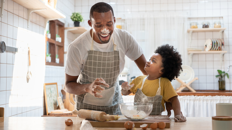 a father and child baking cookies, father has flour of his nose