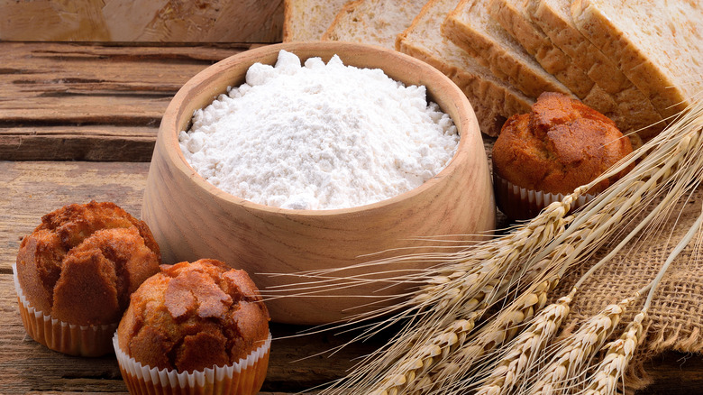 wooden bowl with flour, surrounded by baked muffins and bread