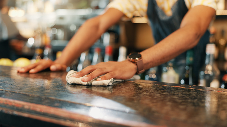 A man's hands wiping the top of a bar with a rag