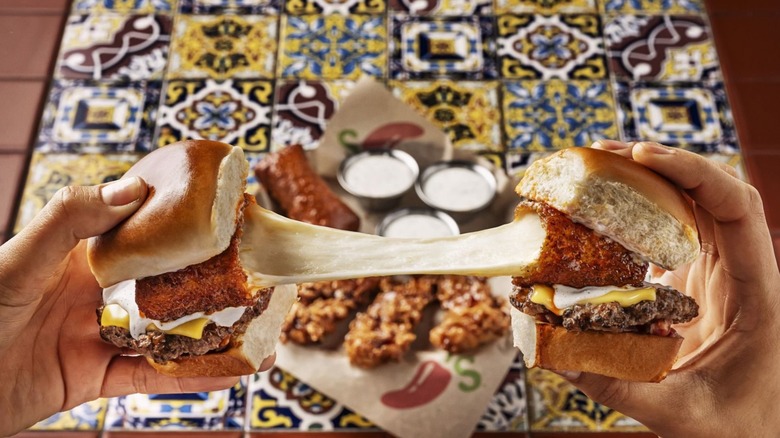 Hands pull apart two burgers stuffed with fried mozzarella in front of Chili's napkin and tiled table