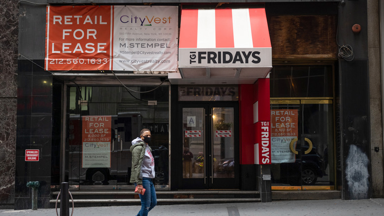 Closed storefront of a TGI Fridays restaurant with person wearing a mask walking by