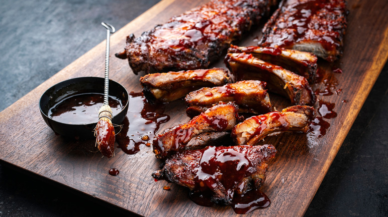 ribs on cutting board with bowl of barbecue sauce and brush