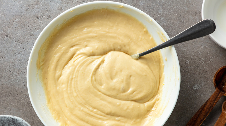 Bowl of pancake batter with metal spoon resting on kitchen counter.