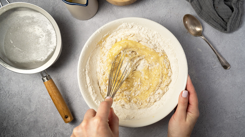 Hands whisking pancake batter in ceramic bowl.