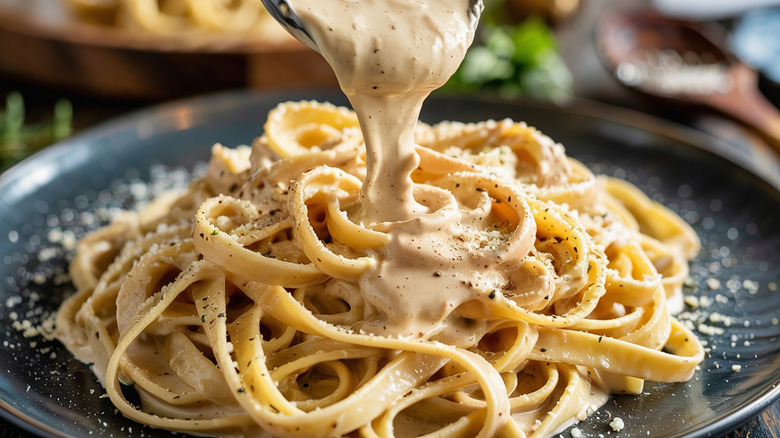 Alfredo sauce being poured over pasta.