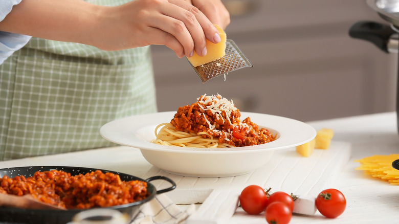 Person grating cheese over spaghetti with tomato sauce