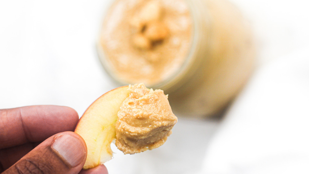 hand holding peanut butter on apple slice