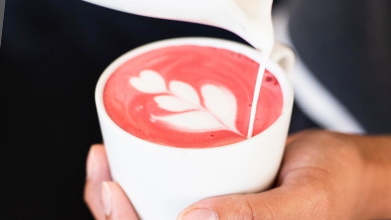 Some barista hands pouring milk on a pink drink in a white cup
