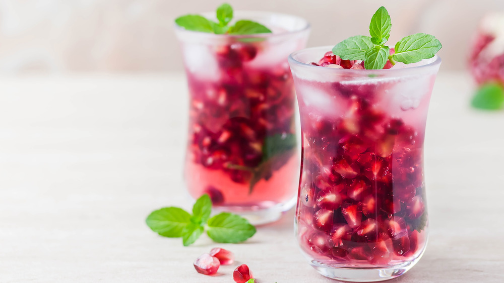 Two glasses filled with pomegranate seeds, cocktail concoction, and topped with mint leaves