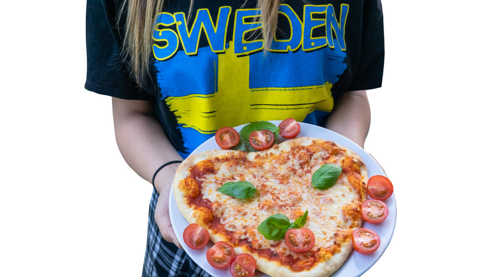 Person wearing Swedish flag t-shirt holding pizza