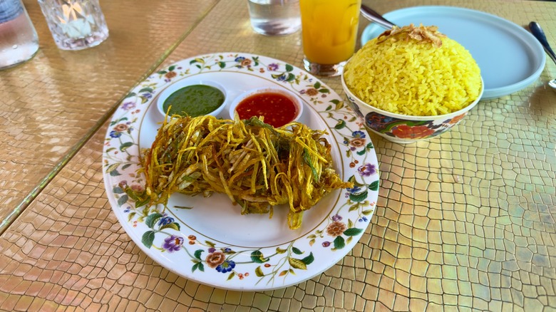 A fritter with dipping sauces next to yellow rice on a gold table