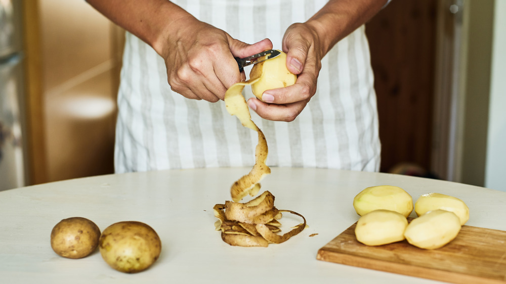A cropped photo of a person peeling potatoes