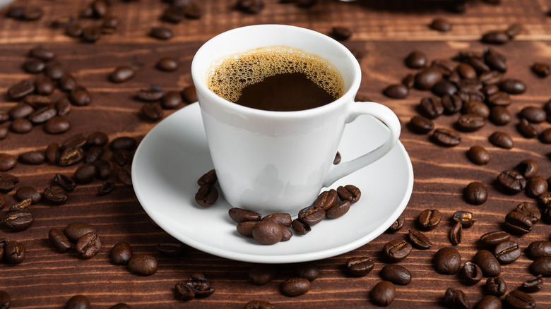 Cup of coffee on a wooden table surrounded by coffee beans