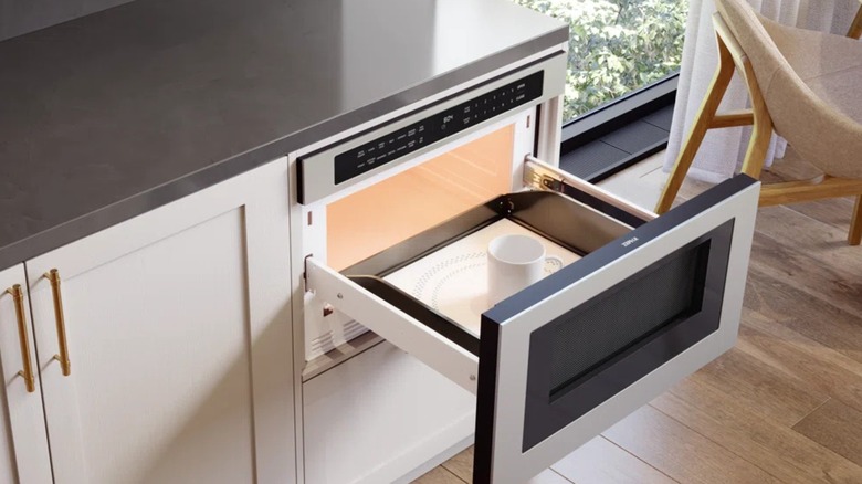 An open microwave drawer with a mug inside