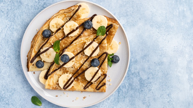 Crepes topped with bananas, blueberries, and chocolate