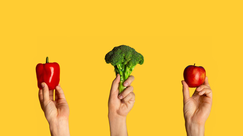 hands holding apple, broccoli and bell pepper