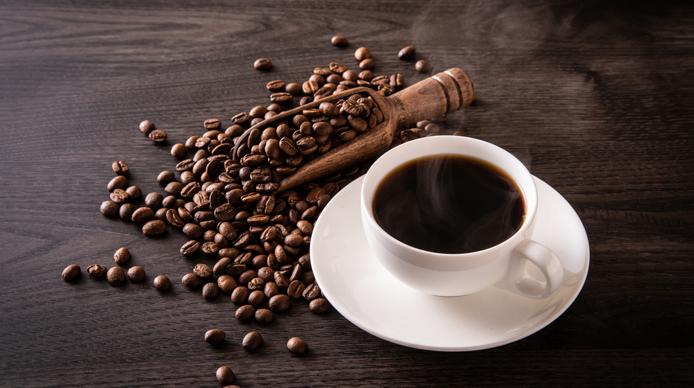 A cup of black coffee surrounded by coffee beans