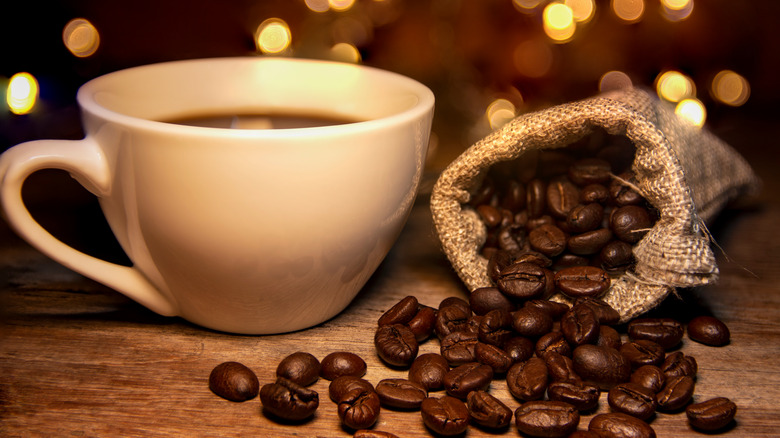 Cup of coffee and roasted coffee beans on table