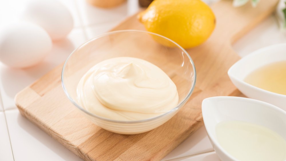 mayonnaise in a glass jar on a cutting board with eggs and lemon