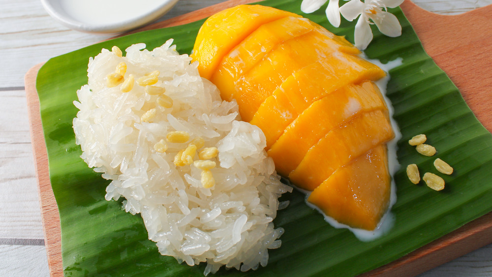 Sticky rice next to mango slices on green sheet