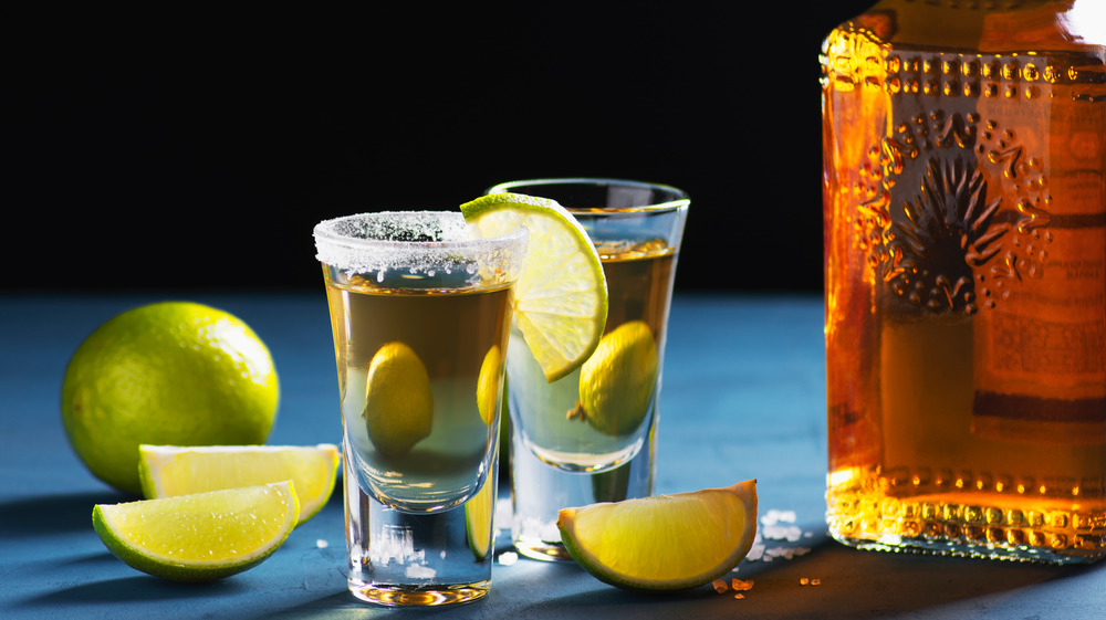 Tequila shots and limes next to a bottle of tequila