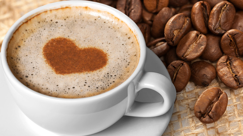 Coffee cup with heart latte art and beans