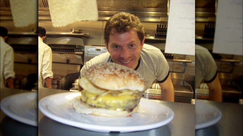 Bobby Flay in a restaurant kitchen with a burger in the window