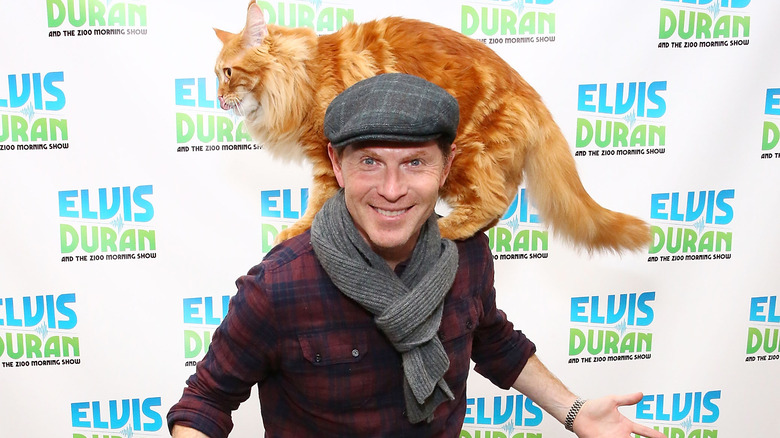Bobby Flay wearing a hat with orange cat on shoulders