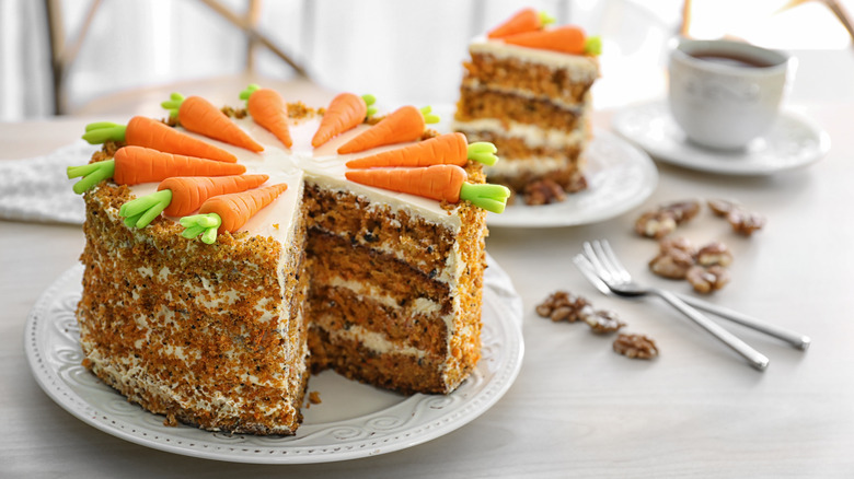 Whole carrot cake on white plate with slice cut out