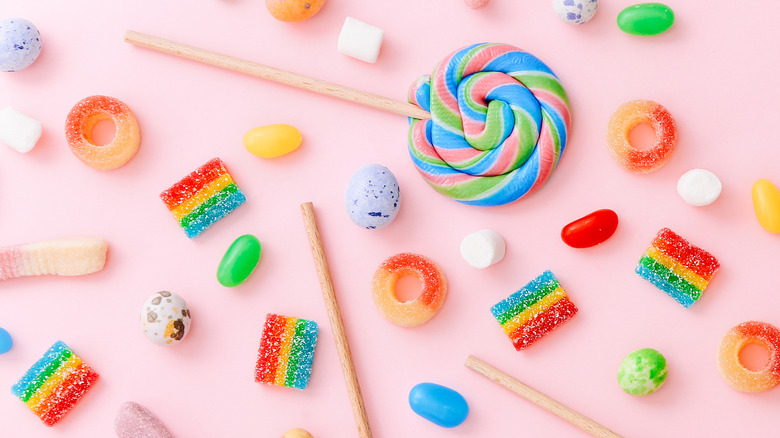 Lollipops, jelly beans, and various gummy candies on pink background