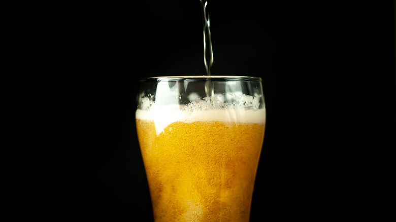 Glass of beer being poured against black background