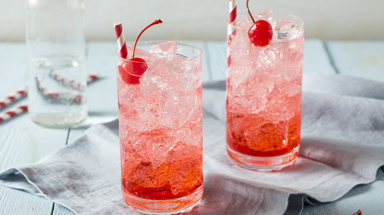 two iced shirley temples with cherries on top and paper straws