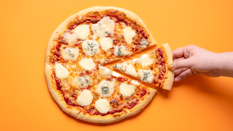 Hand grabbing slice of pizza on orange background