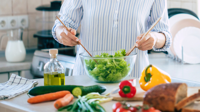 Person making a salad in a clear bowl