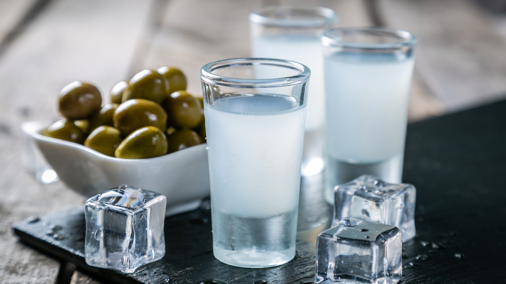 Shots of ouzo on a table with ice and olives