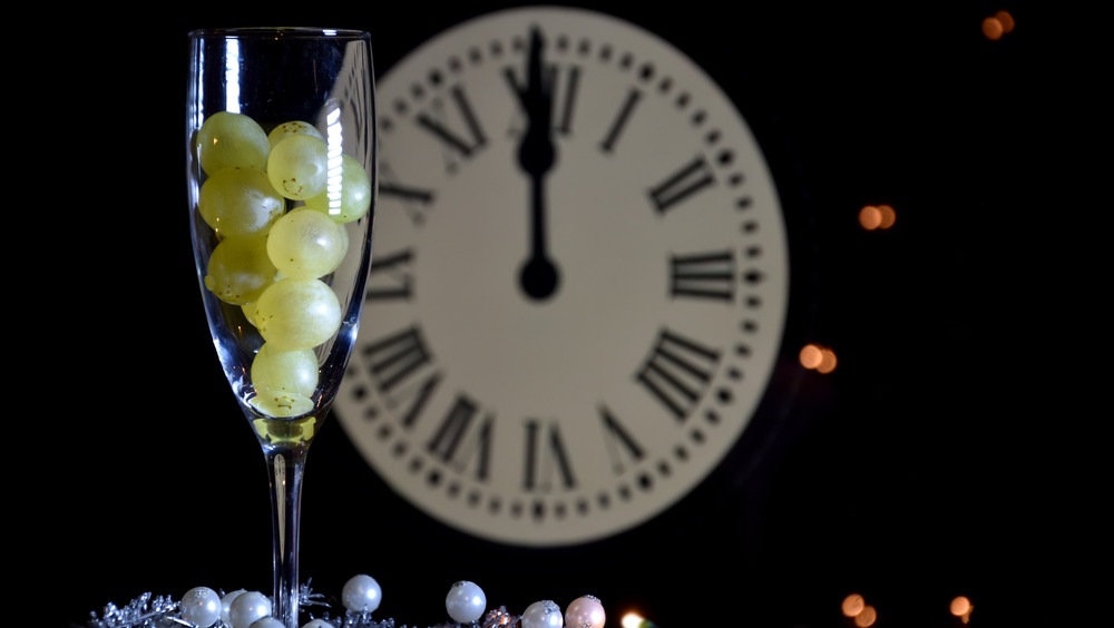 Champagne glass filled with grapes next to clock