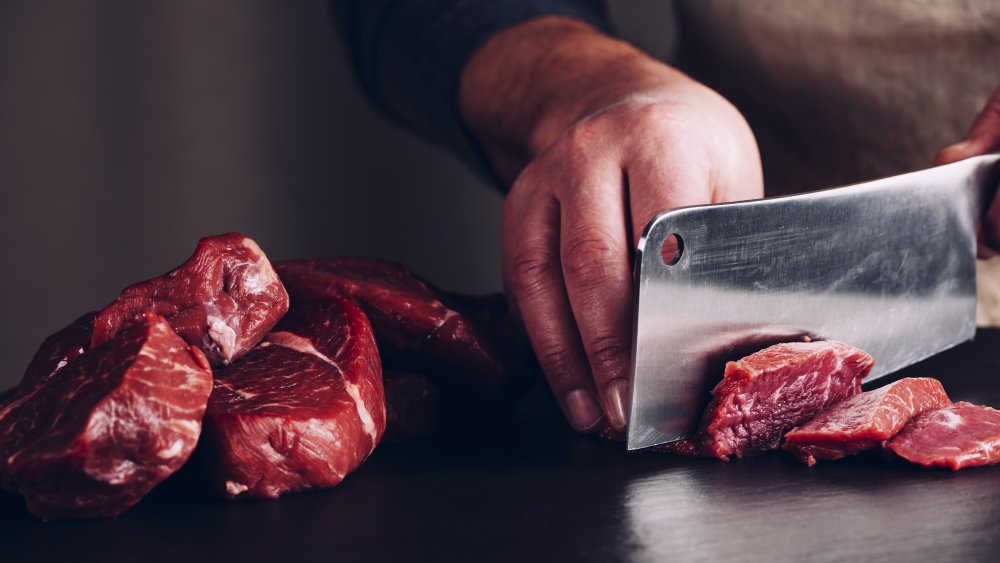 Hand of chef and butcher knife chopping up raw steak