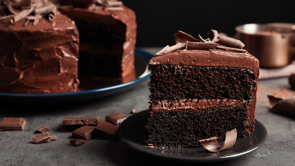 slice of chocolate cake on a plate with the rest of the chocolate cake in the background 