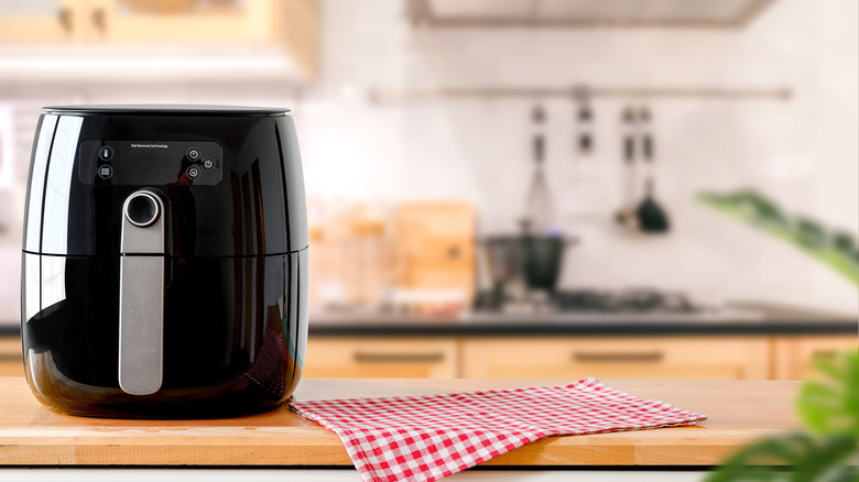 black air fryer on kitchen counter next to red and white checkered cloth