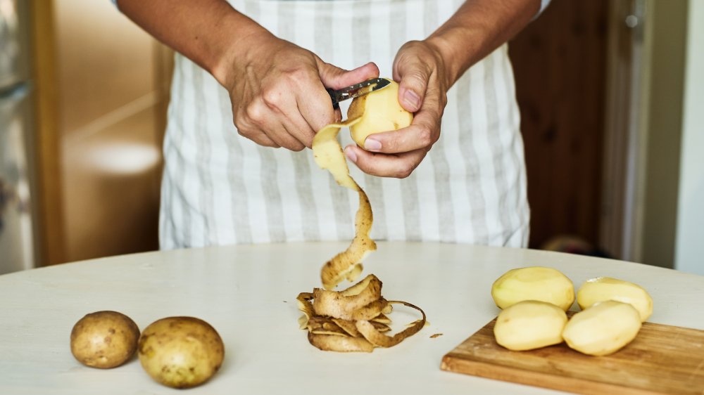person peeling potatoes at a white table