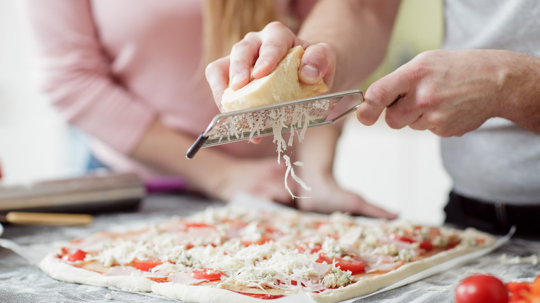 Grating cheese onto pizza