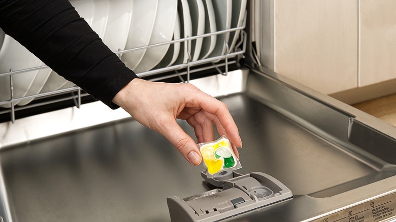 Open dishwasher with hand putting soap in slot 