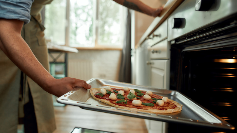 person putting pizza into oven 