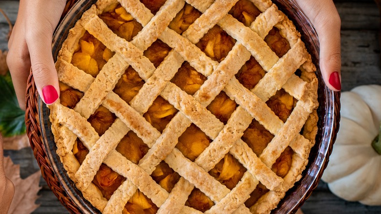 A person holding a lattice crust pie in a baking dish