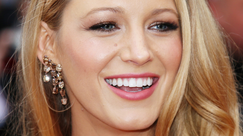 A close-up of Blake Lively smiling with sparkly eye shadow and dazzling earrings