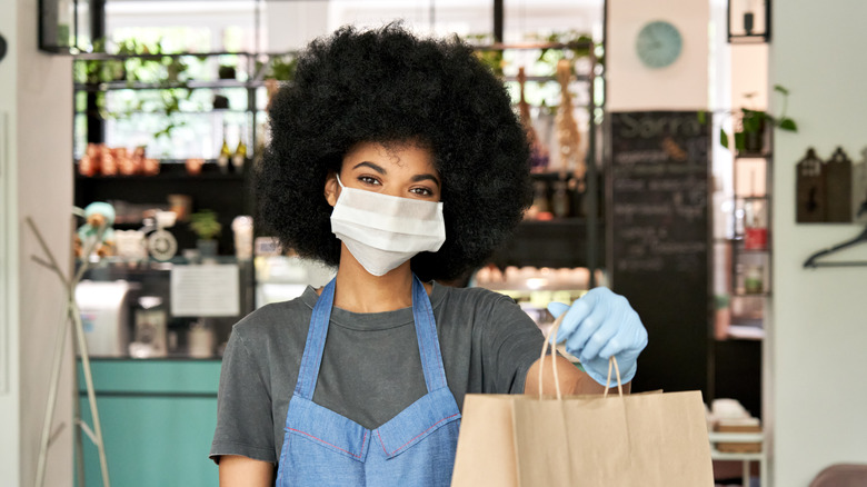 A masked worker handing over a bag of food