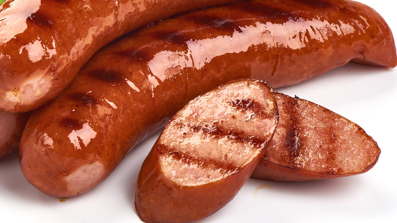 Two slices of grilled brats next to two whole grilled brats